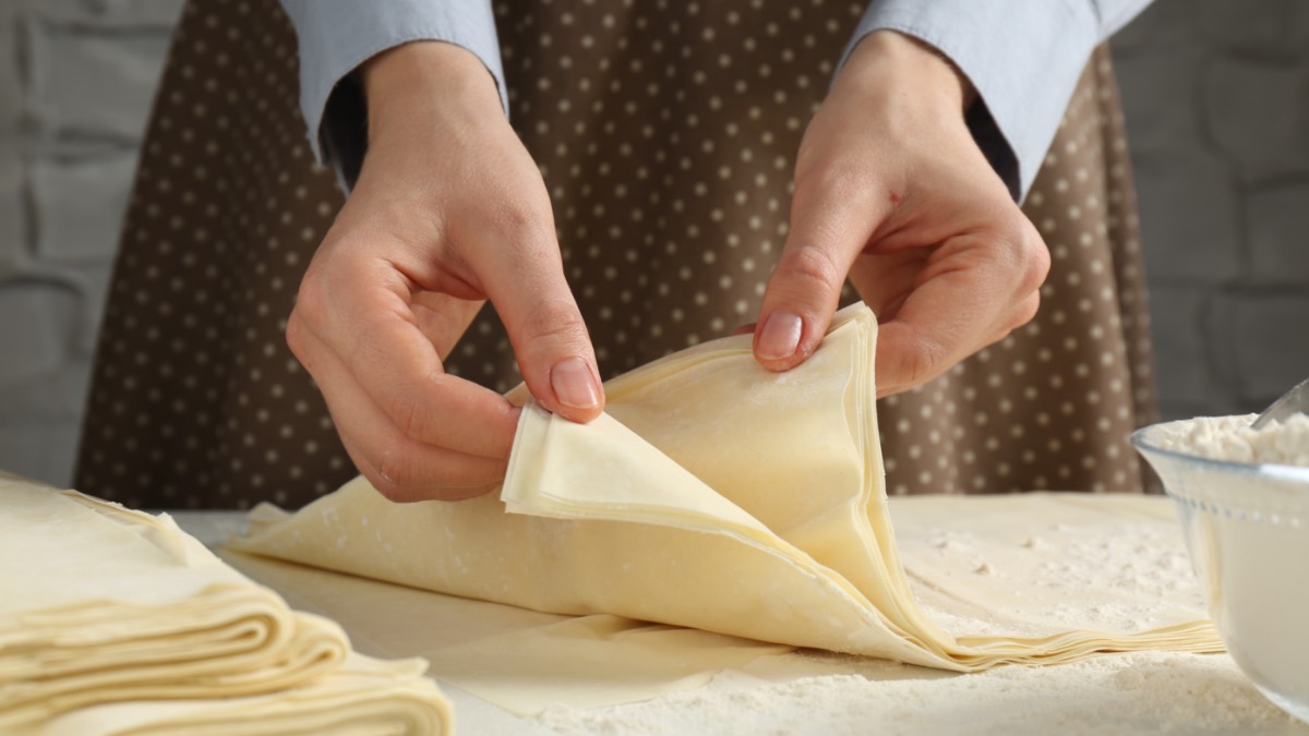 Tipps fürs Backen mit Blätterteig: Eine Frau zieht mehrere, übereinander gelegte Blätterteige mit den Händen auseinander.