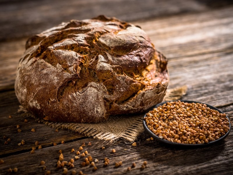 Buchweizen-Quark-Brot mit umherliegenden Buchweizenkörnern auf einem Holztisch.