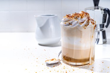Glas mit Crème-brûlée-Latte, Espressokocher im Hintergrund