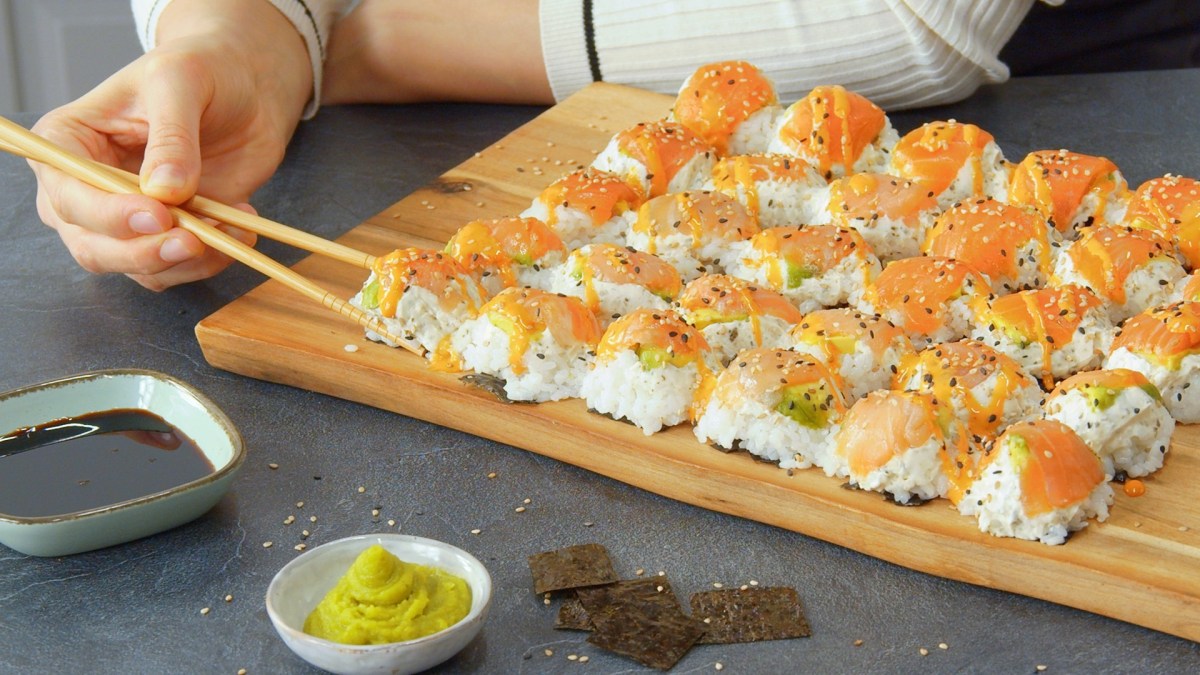 Jemand isst Eierkarton-Sushi von einem Holzbrett mit zwei Esstäbchen.