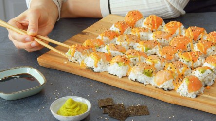 Jemand isst Eierkarton-Sushi von einem Holzbrett mit zwei Esstäbchen.