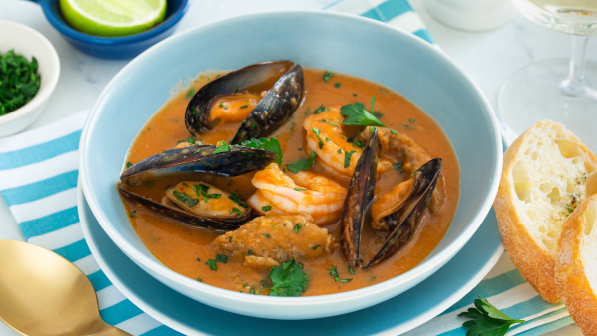 Eine Schüssel mit französischer Fischsuppe Bouillabaisse. Daneben 2 Scheiben Baguette.