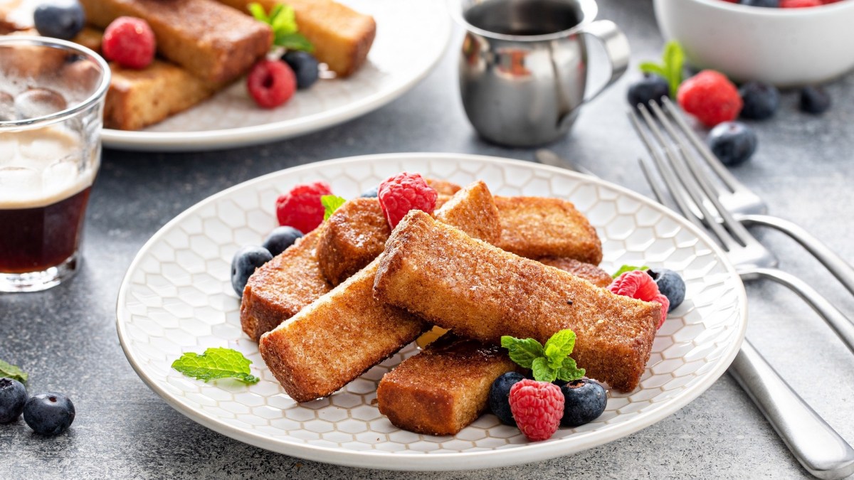 French-Toast-Stangen auf zwei Tellern, garniert mit Beeren, daneben Besteck.