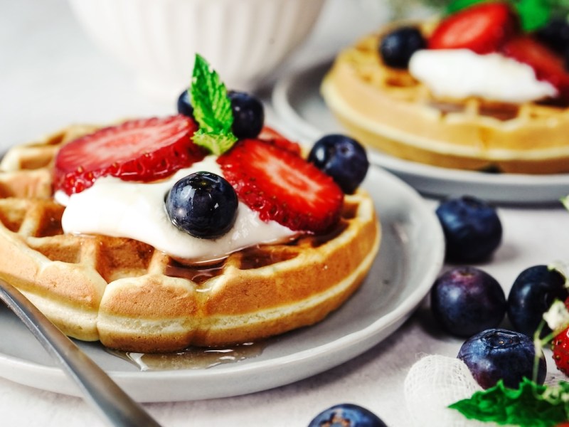 2 Teller mit je einer Frischkäse-Waffel getoppt mit Schmand, Beeren und Ahornsirup.