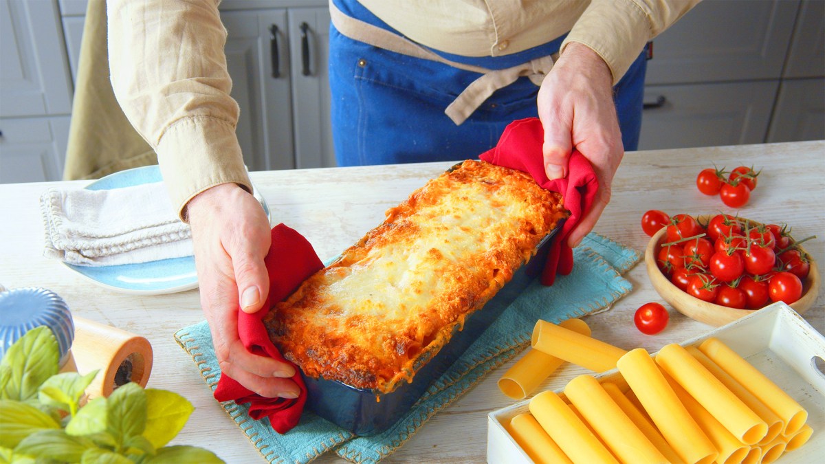 Ein Koch präsentiert eine Kastenform mit gefüllten Cannelloni mit Mozzarella.