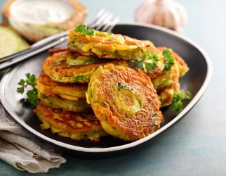 Gemüse-Rösti auf einem dunklen Teller, garniert mit krauser Petersilie.