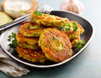 Gemüse-Rösti auf einem dunklen Teller, garniert mit krauser Petersilie.