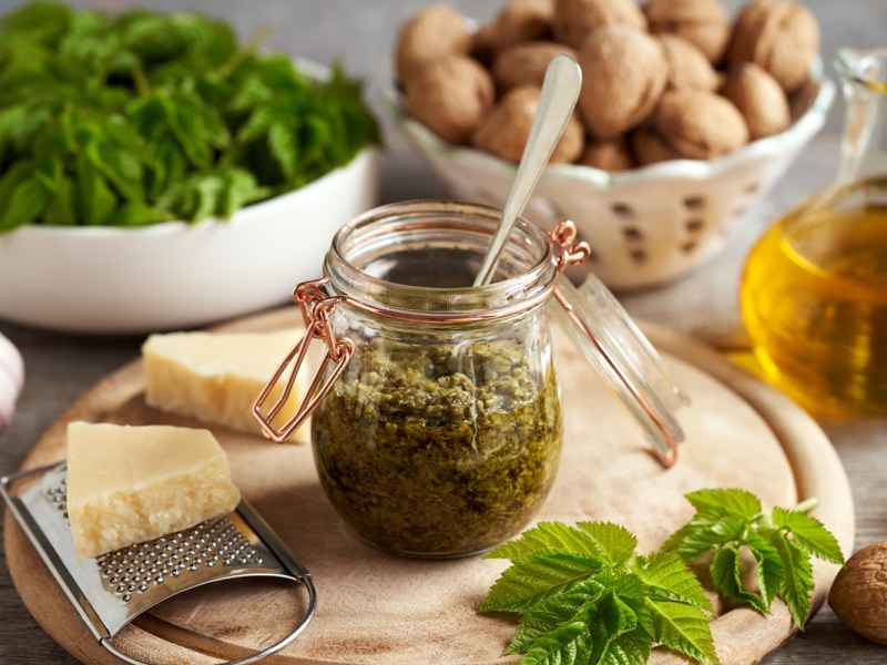 Giersch-Pesto in einem Glas, inmitten von Zutaten wie Parmesan, Walnüssen und Olivenöl.