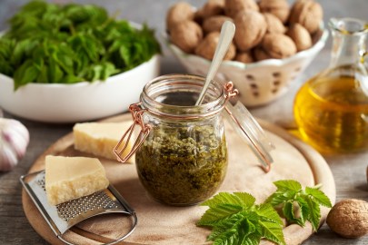 Giersch-Pesto in einem Glas, inmitten von Zutaten wie Parmesan, Walnüssen und Olivenöl.