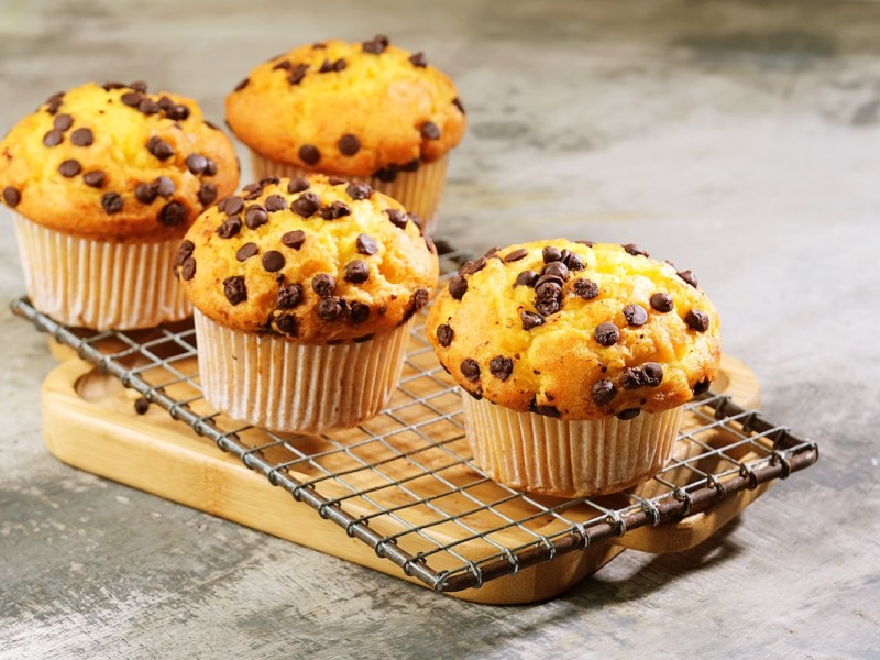 4 Haferflocken-Schoko-Muffins auf einem Kuchengitter, das auf einem Holzbrett steht.