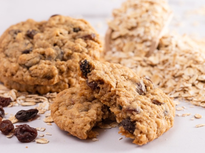 Mehrere zuckerfeie Haferflockenkekse mit Joghurt und Rosinen. Daneben finden sich Zutaten.