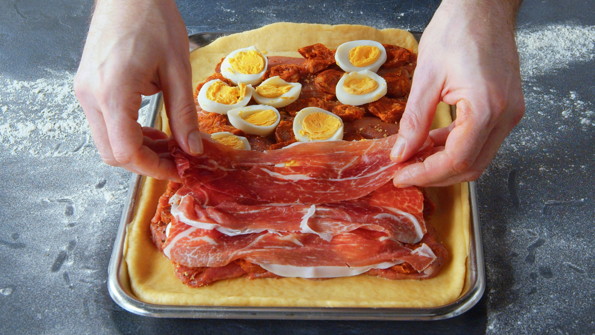 Ein Koch belegt den Boden einer spanischen Fleischpastete mit Schinken.