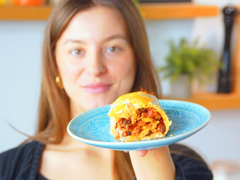 Unsere Showköchin hält eine Käsekartoffelrolle auf einem blauen Teller in die Kamera.