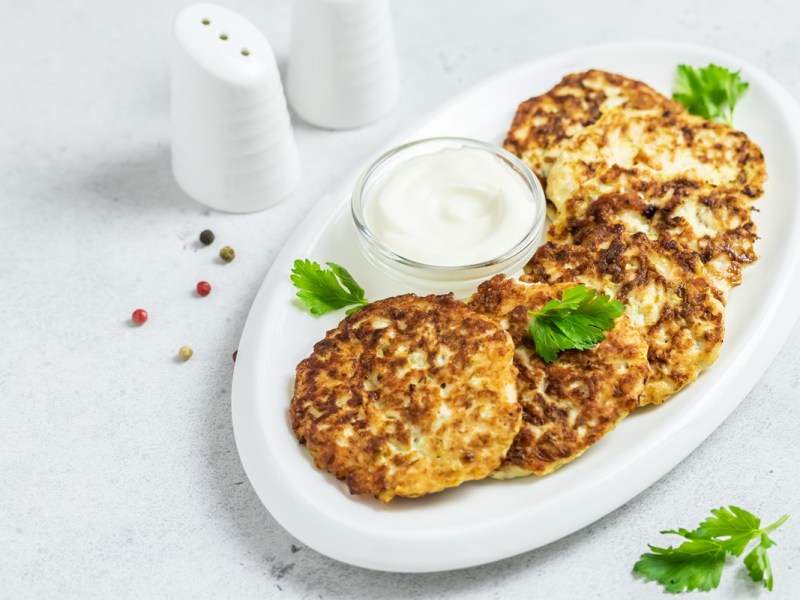 Mehrere Kartoffel-Feta-Puffer auf einem ovalen Teller, serviert mit Dip.