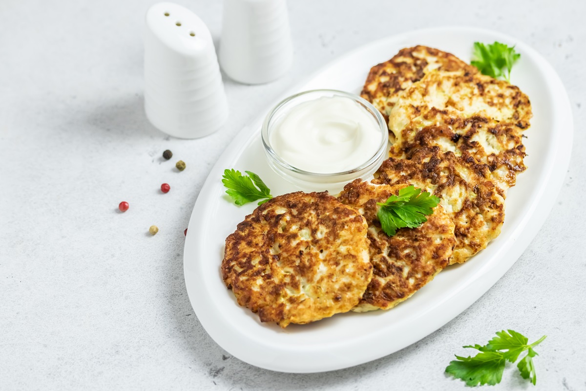 Mehrere Kartoffel-Feta-Puffer auf einem ovalen Teller, serviert mit Dip.