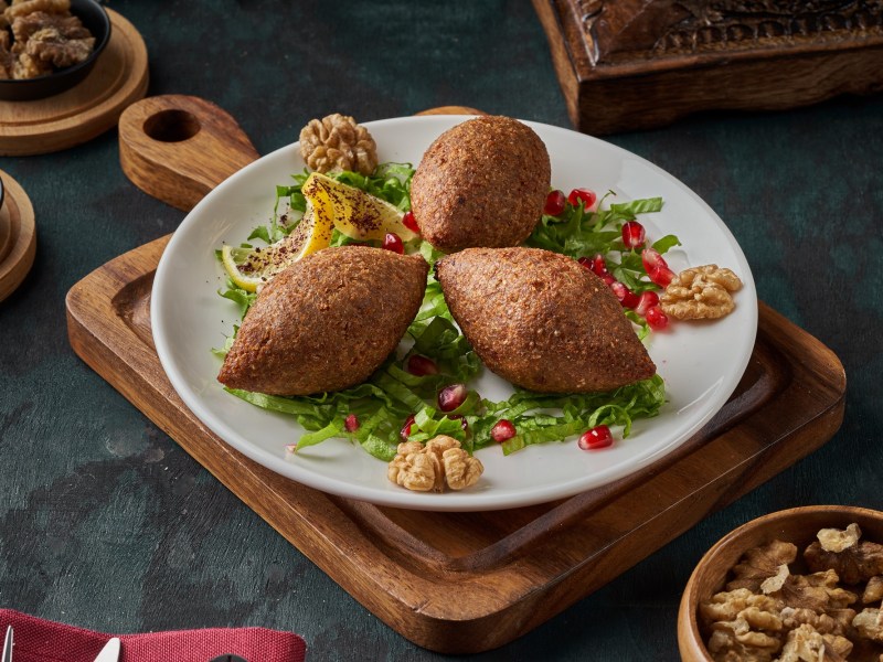 Drei levantinische Kibbeh: Bulgur-Hackfleisch-Bällchen auf einem Teller, serviert mit Zitrone.