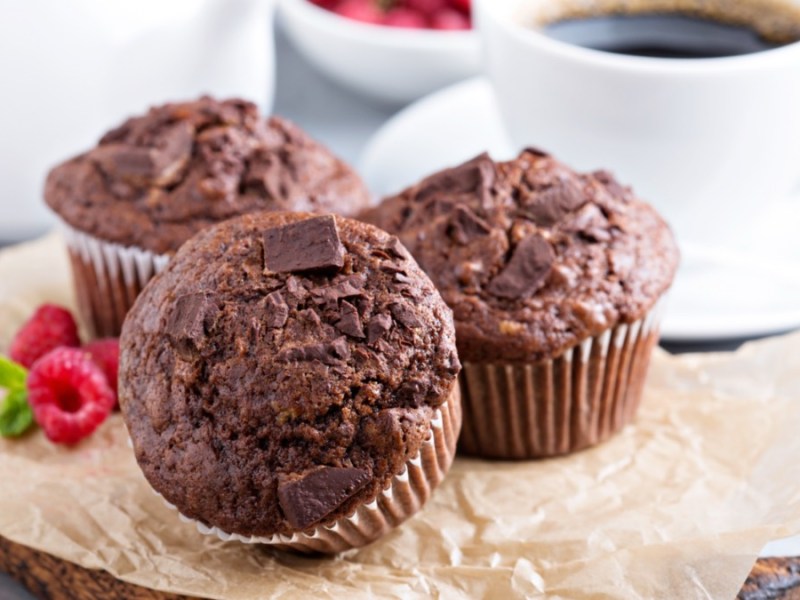 Drei Marshmallow-Muffins auf einem Stück Backpapier. Im Hintergrund steht eine Tasse Kaffee.