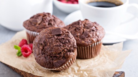Drei Marshmallow-Muffins auf einem Stück Backpapier. Im Hintergrund steht eine Tasse Kaffee.