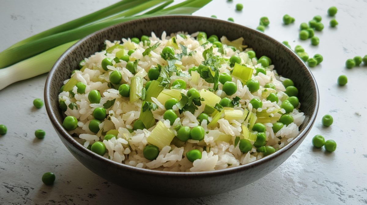 Eine Schüssel Reis mit Lauch und Erbsen, drumherum einige Erbsen und Lauchstangen.