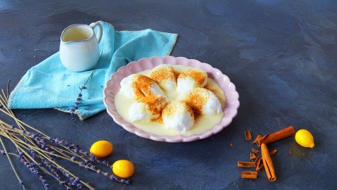 Ein rosa Teller mit Farófias. Dahinter liegt ein blaues Tuch auf dem eine kleine Kanne steht. Im Vordergrund liegen noch einige kleine Zwiebeln, Zimtstangen und Blumen.