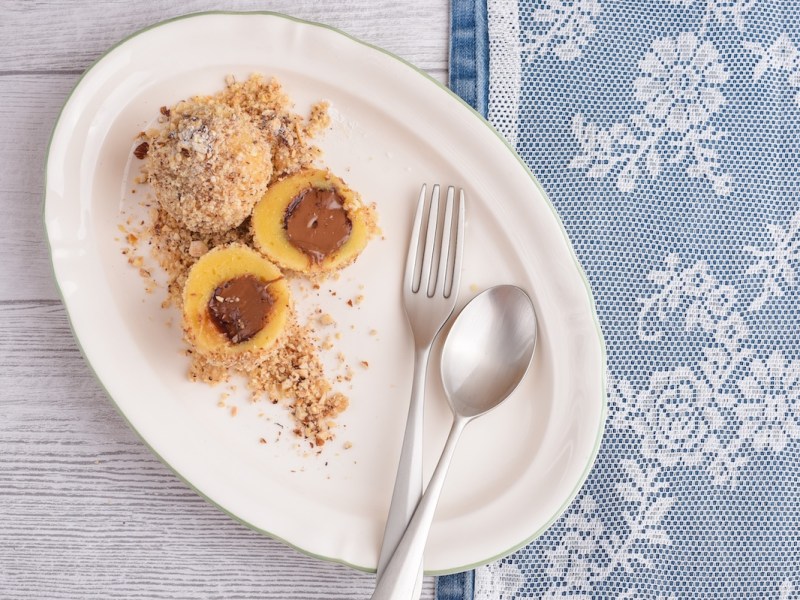 Schoko-Quark-Klöße, einer aufgeschnitten, mit Besteck auf einem ovalen Teller in der Draufsicht.