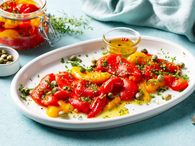 Ein Teller Antipasti-Paprika mit Kapern und Kräutern auf einem blauen Hintergrund.
