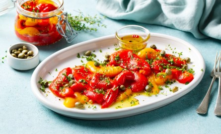 Ein Teller Antipasti-Paprika mit Kapern und Kräutern auf einem blauen Hintergrund.