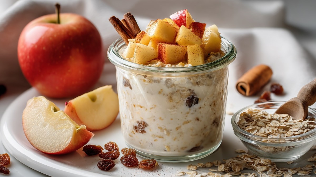 Apfel-Zimt-Overnight-Oats in einem Glas getoppf mit Apfelstückchen. Drumherum einige Zutaten.