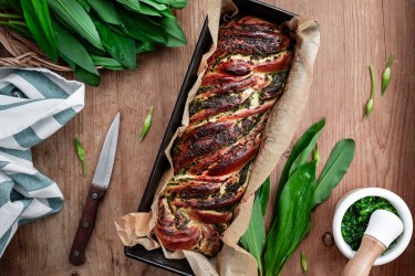 Bärlauch-Hefezopf in einer Kastenform. Daneben liegt Bärlauch sowie ein Messer.