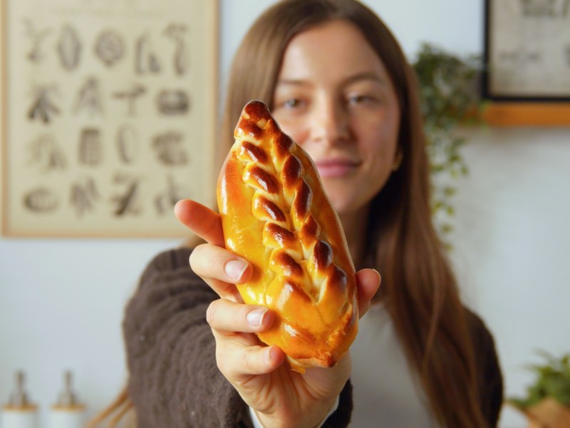Eine Köchin hält ein gefülltes Brioche-Brötchen in die Kamera.