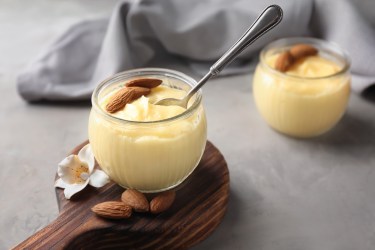 2 Gläser Eierlikör-Creme garniert mit Mandeln, in einer steckt ein Löffel. Dahinter eine Stoffserviette.
