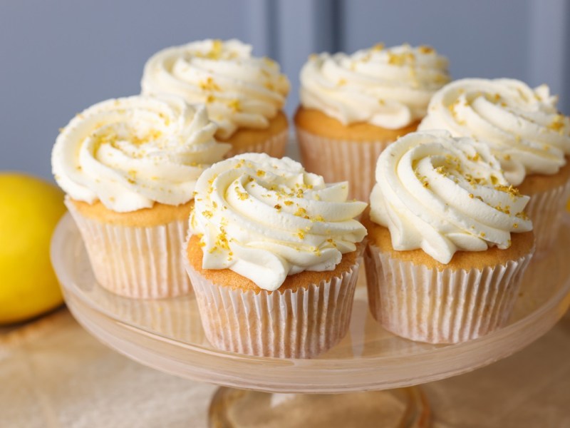 Eierlikör-Cupcakes auf einem Tortenständer. Im Hintergrund liegt eine Zitrone.