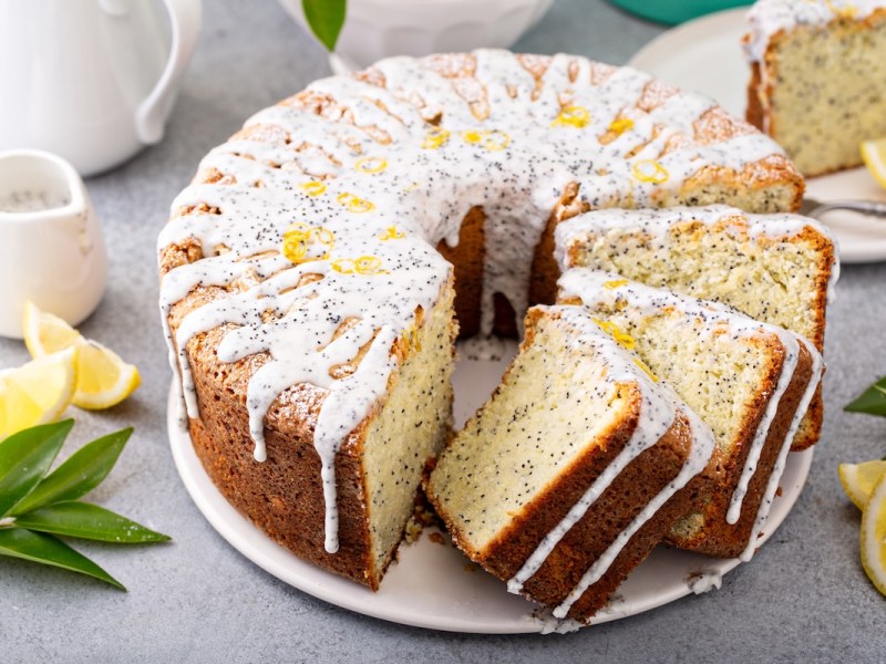 Ein angeschnittener Eierlikör-Gugelhupf mit Mohn und Zuckerguss, daneben ein paar Zitronenscheiben und Kännchen.