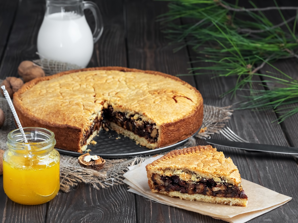 Engadiner Nusstorte auf einem Kuchenblech. Ein Stück wurde herausgeschnitten und liegt im Vordergrund.