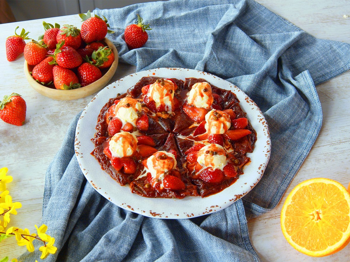 Ein Teller mit Erdbeer-Crêpes mit grünem Pfeffer, darauf mehrere Kugeln Vanilleeis.
