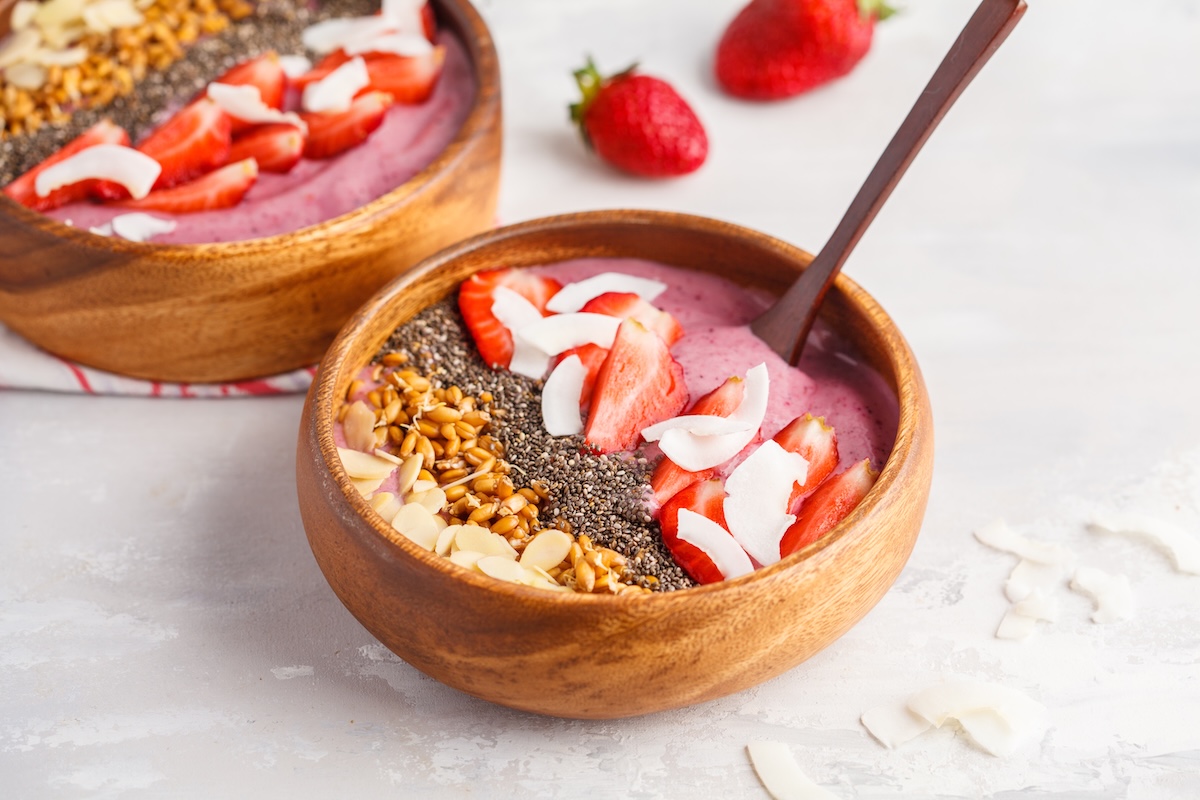2 Erdbeer-Smoothie-Bowls mit Banan, garniert mit Erdbeeren, Nüssen und mehr.