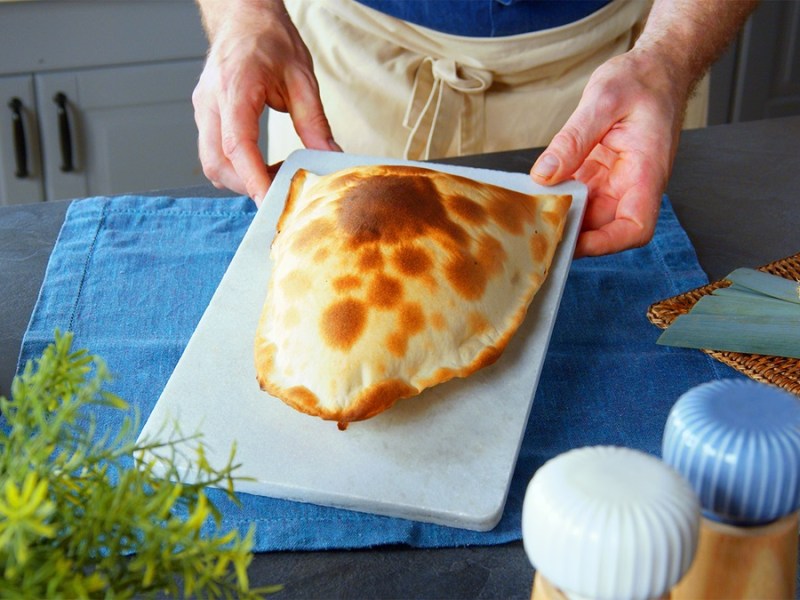 Eine Flammkuchentasche wird auf einem Brett präsentiert.