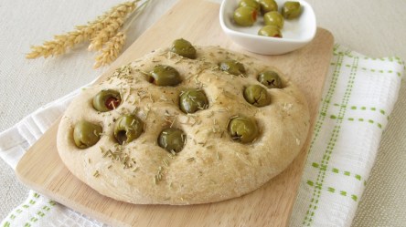 Eine Focaccia mit Oliven auf einem Holzbrett.