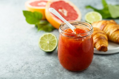 Glas mit Grapefruit-Limetten-Marmelade, Grapefruit, Limetten und Croissant daneben.