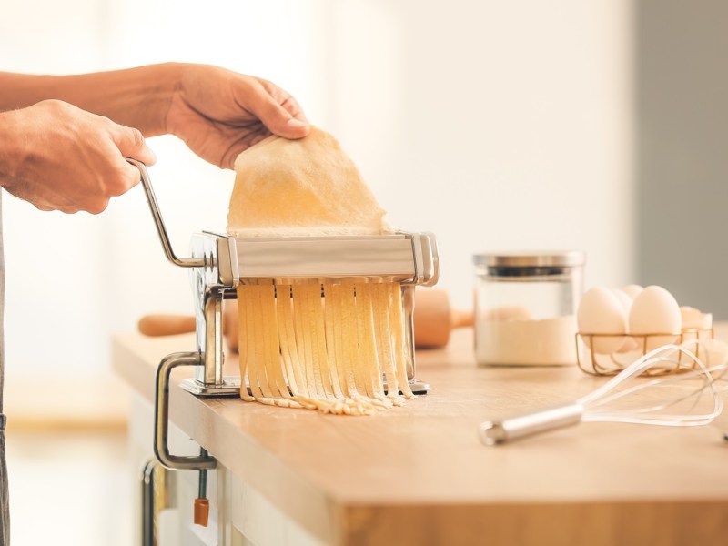Eine Person dreht italienischen Nudelteig durch eine Nudelmaschine.