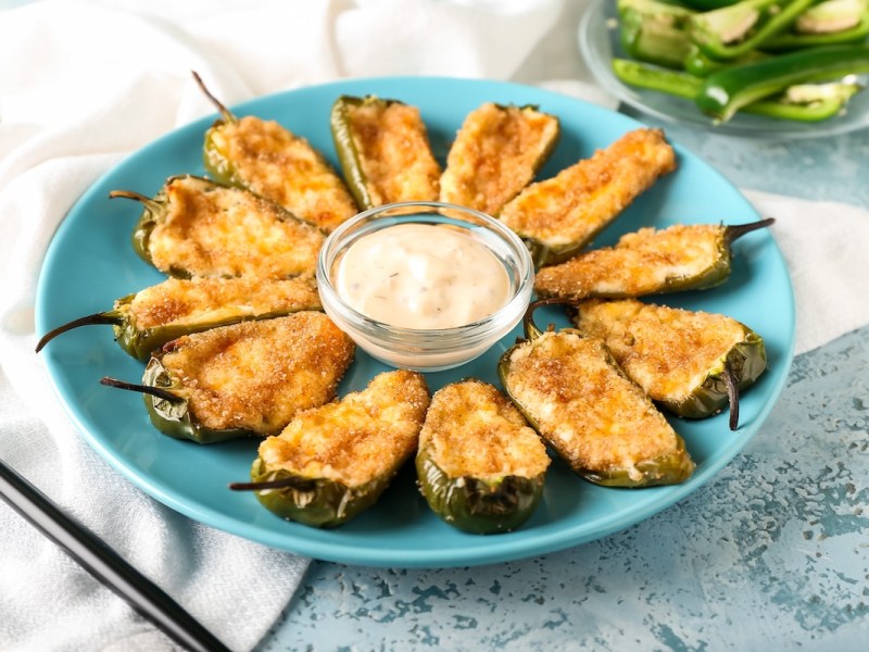 Ein Teller mit Jalapeño Poppers, überbackene grüne Chilischoten, in der Mitte steht eine Dip-Schale.