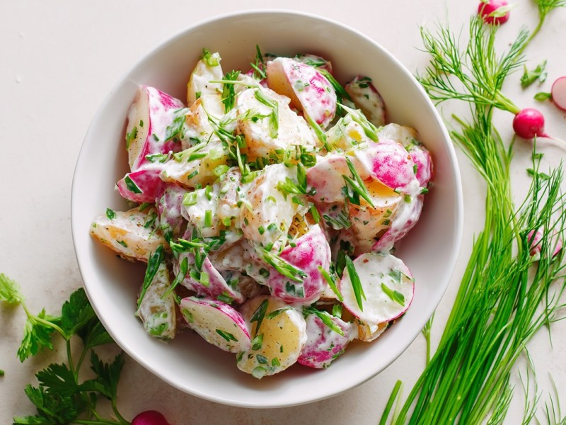 Schale mit Kartoffel-Radieschen-Salat und Kräuter daneben