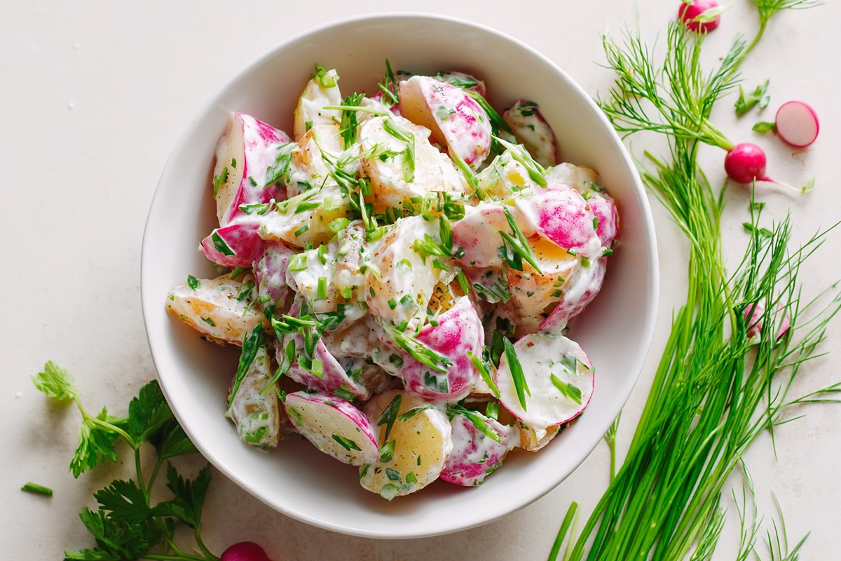 Schale mit Kartoffel-Radieschen-Salat und Kräuter daneben