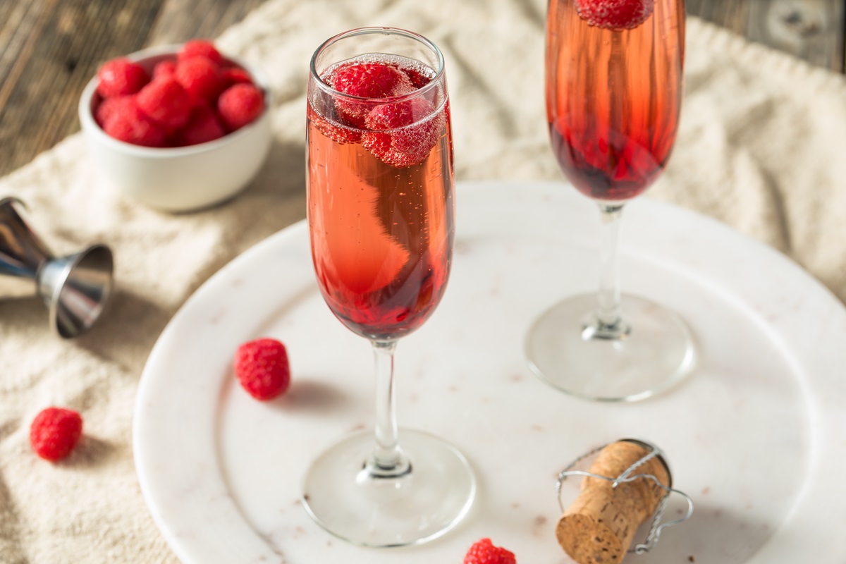 Zwei Gläser Kir Royal mit Himbeeren auf einem weißen Marmortablett.