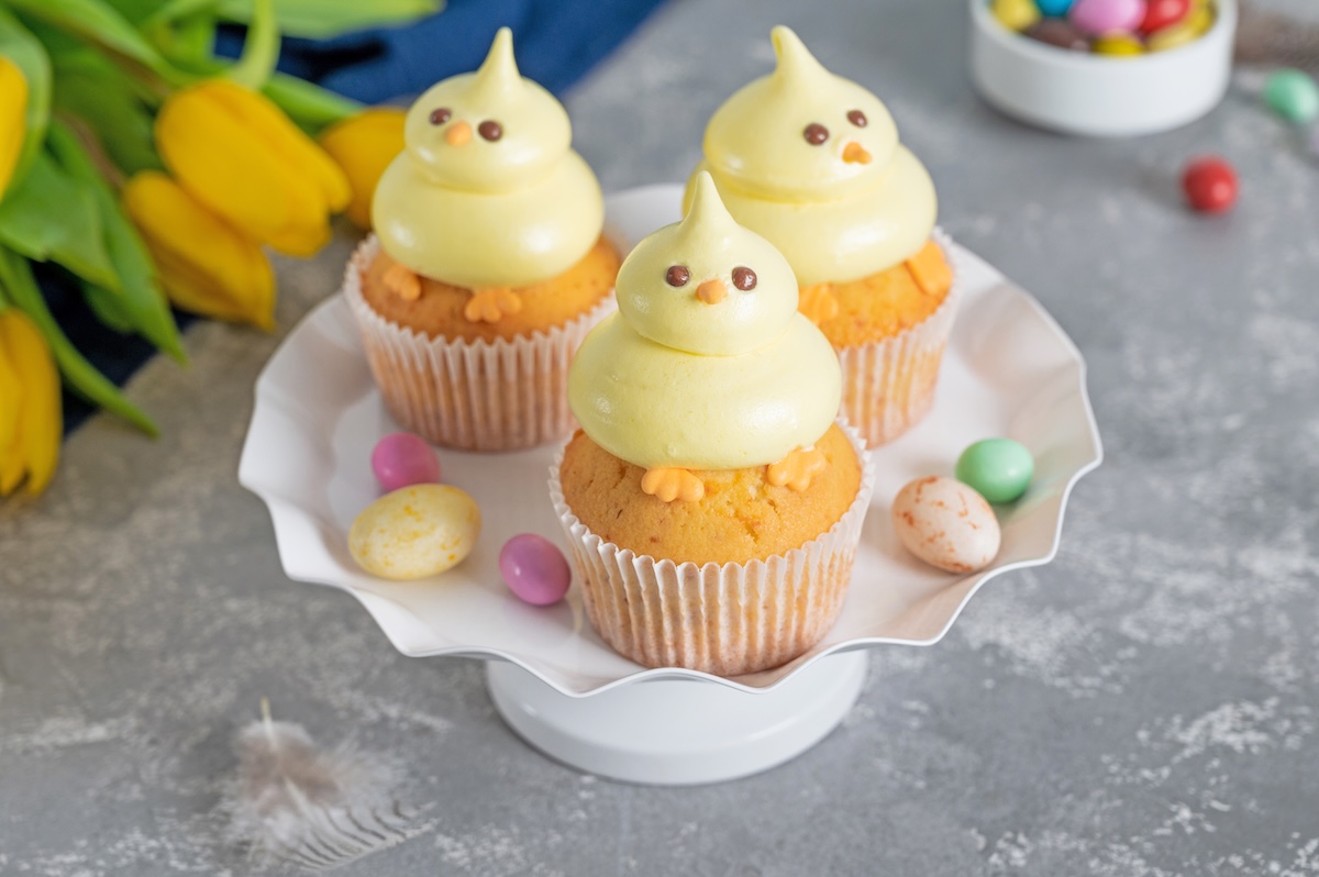 3 Küken-Cupcakes auf einem Teller, drumherum Osterdeko und Tulpen.
