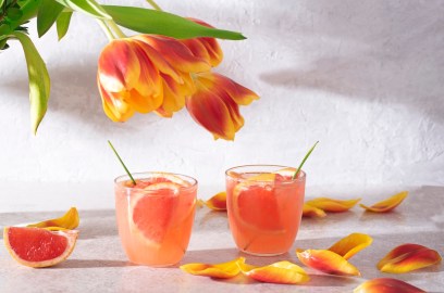 2 Gläser Martini Tonic garniert mit frischer Grapefruit, daneben ein paar Tulpen.