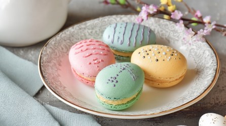 Ein Teller mit 4 Osterei-Macarons, die mit Zuckerschrift verziert wurden.