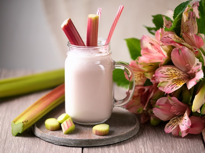 Glas mit Rhabarber-Lassi und Rhabarberstangen auf einem Tisch