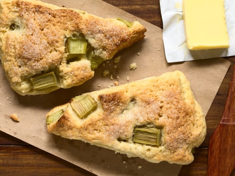 Zwei Rhabarber-Scones in der Draufsicht. Daneben ein Stück Butter.