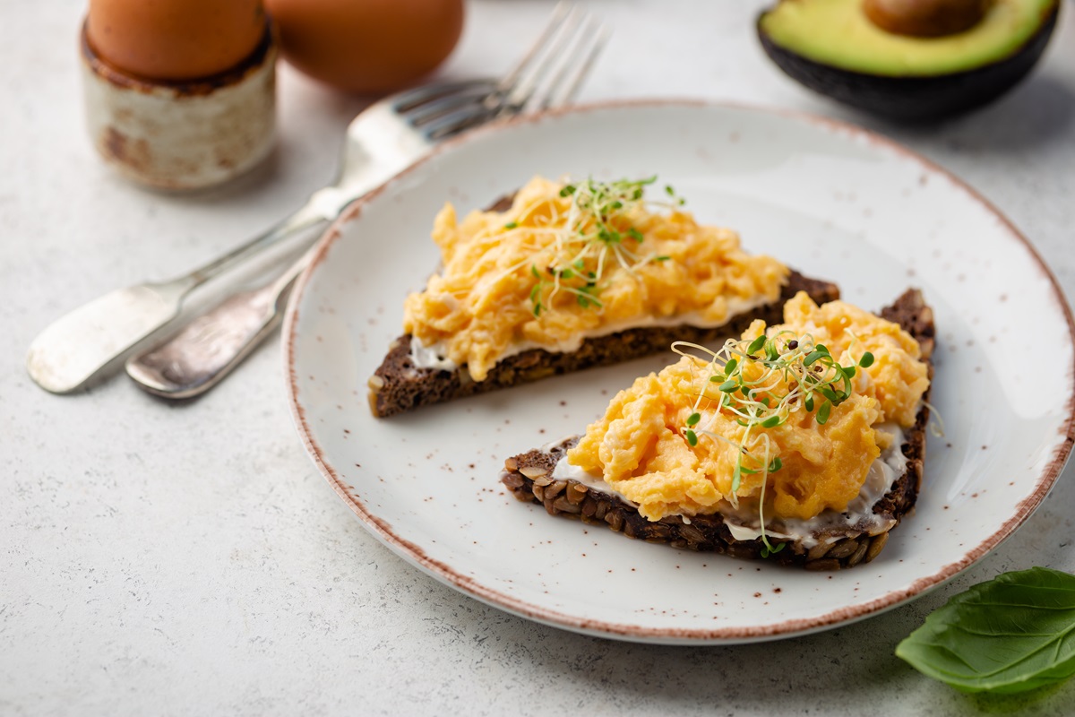 Zwei Brotscheiben mit Rührei mit Quark auf einem hellen Teller. Das Ei ist mit Sprossen garniert.